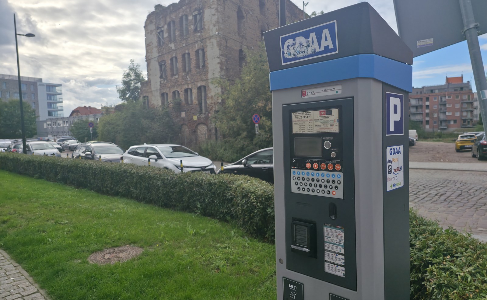 Parkscheinautomat in der Danziger Parkzone auf der Speicherinsel, dahinter eine Speicherruine und geparkte Autos